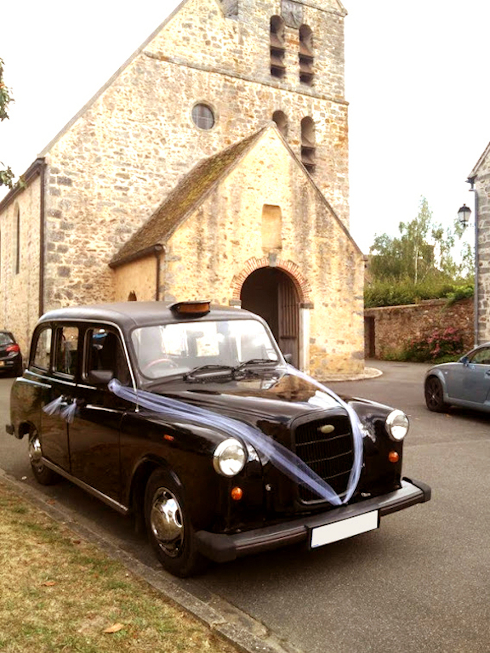 taxi anglais noir devant église décorations tulles blancs enjoliveurs chromés vue trois quart avant droite