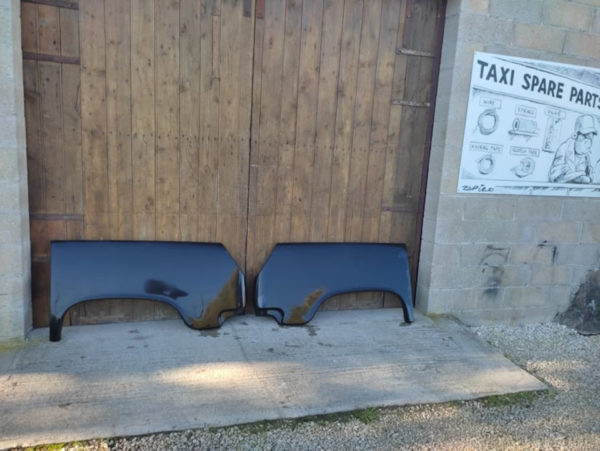 deux ailes arrieres noirs de taxi anglais poses devant porte garage en bois