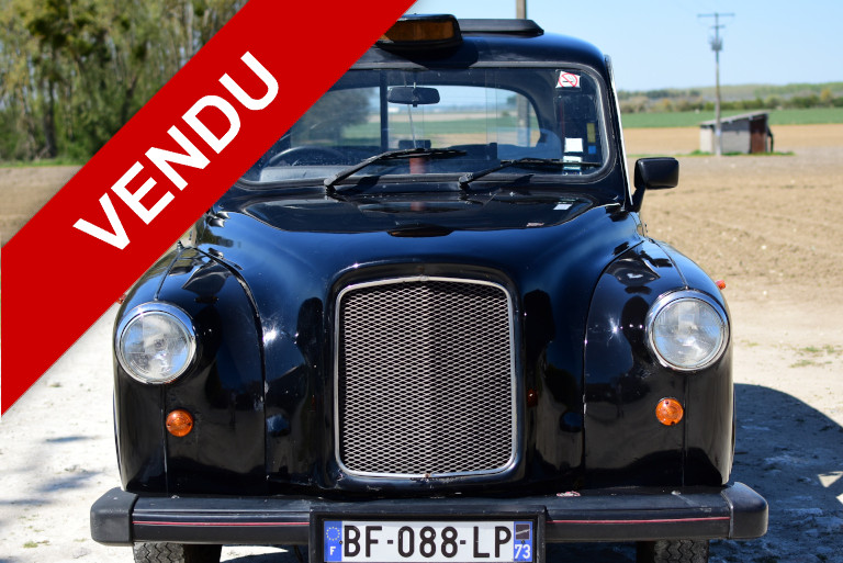 taxi anglais noir vue de face avec un bandeau rouge et blanc vendu